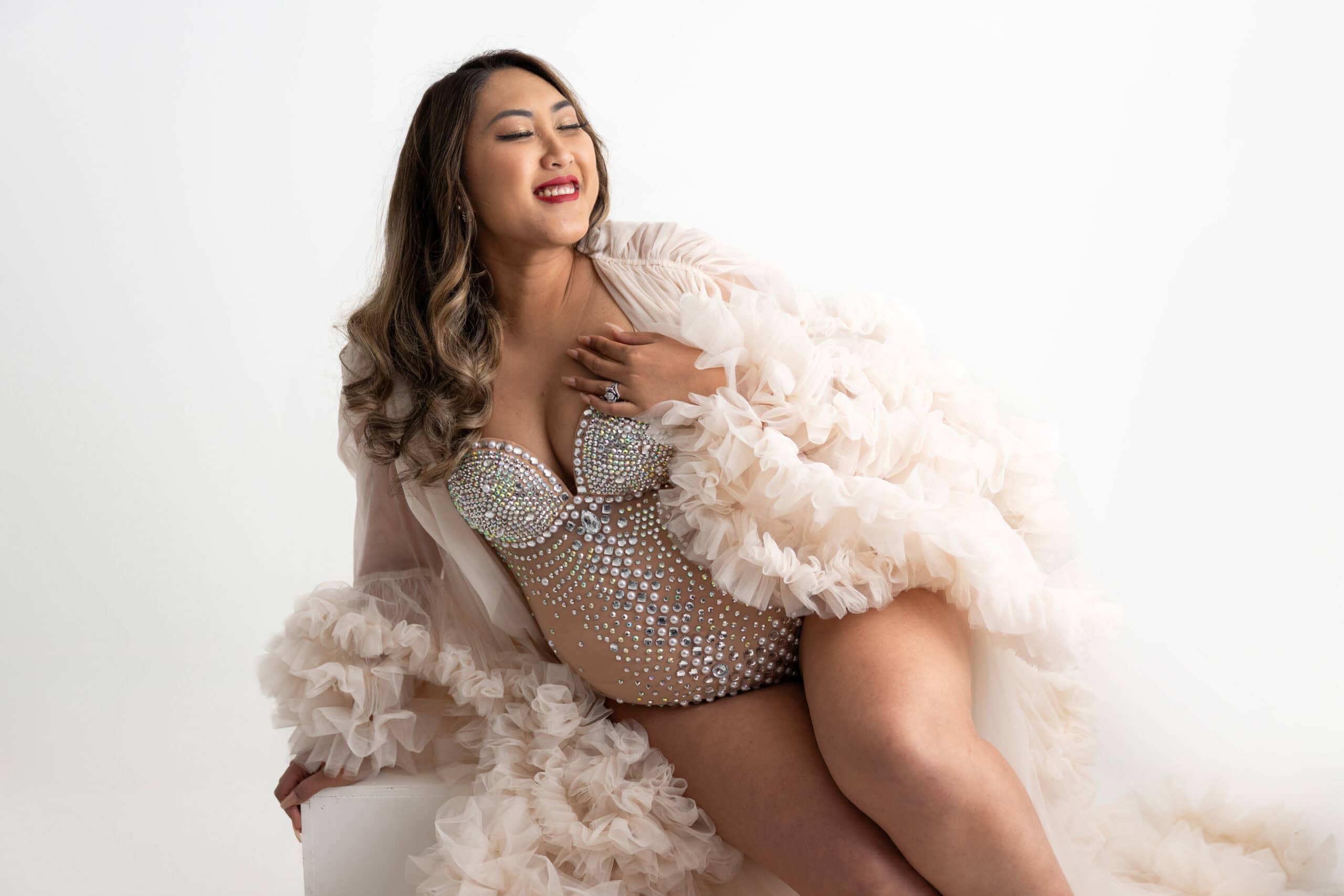 Pregnant women sitting on her side, dressed in a rhinestone body suit and robe.