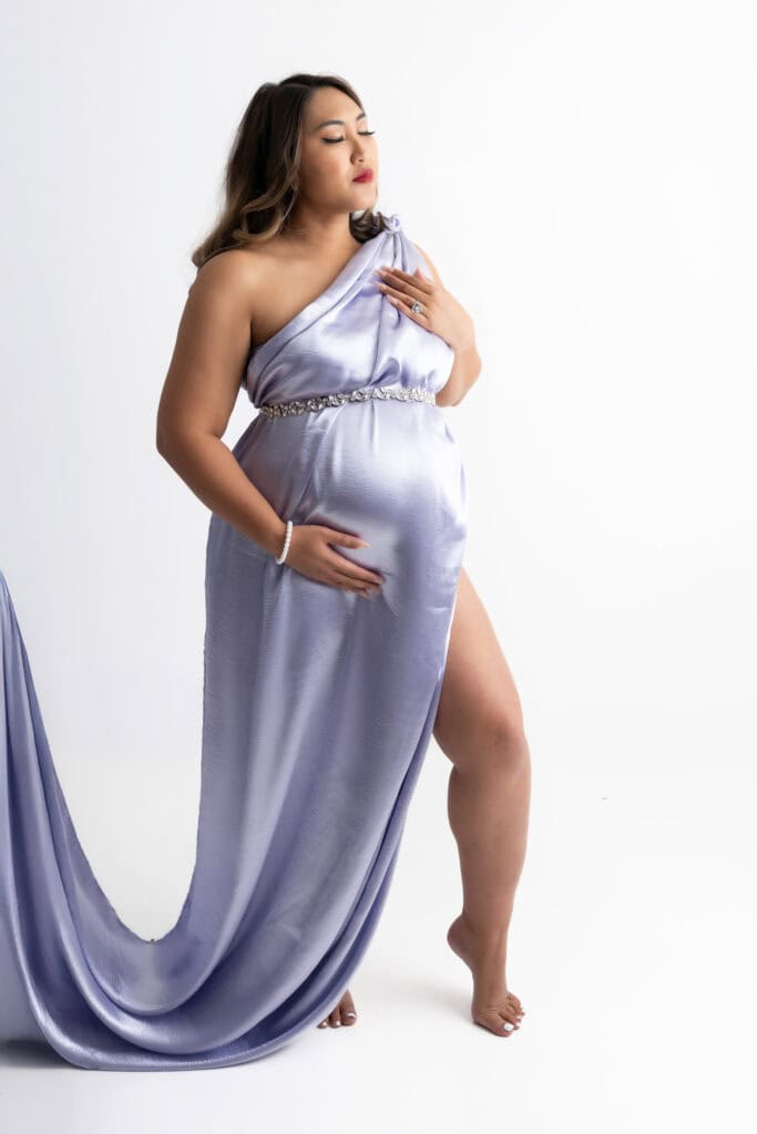 Pregnant women draped in a lilac silk fabric, caressing her pregnant belly in a photography studio in Chicago.