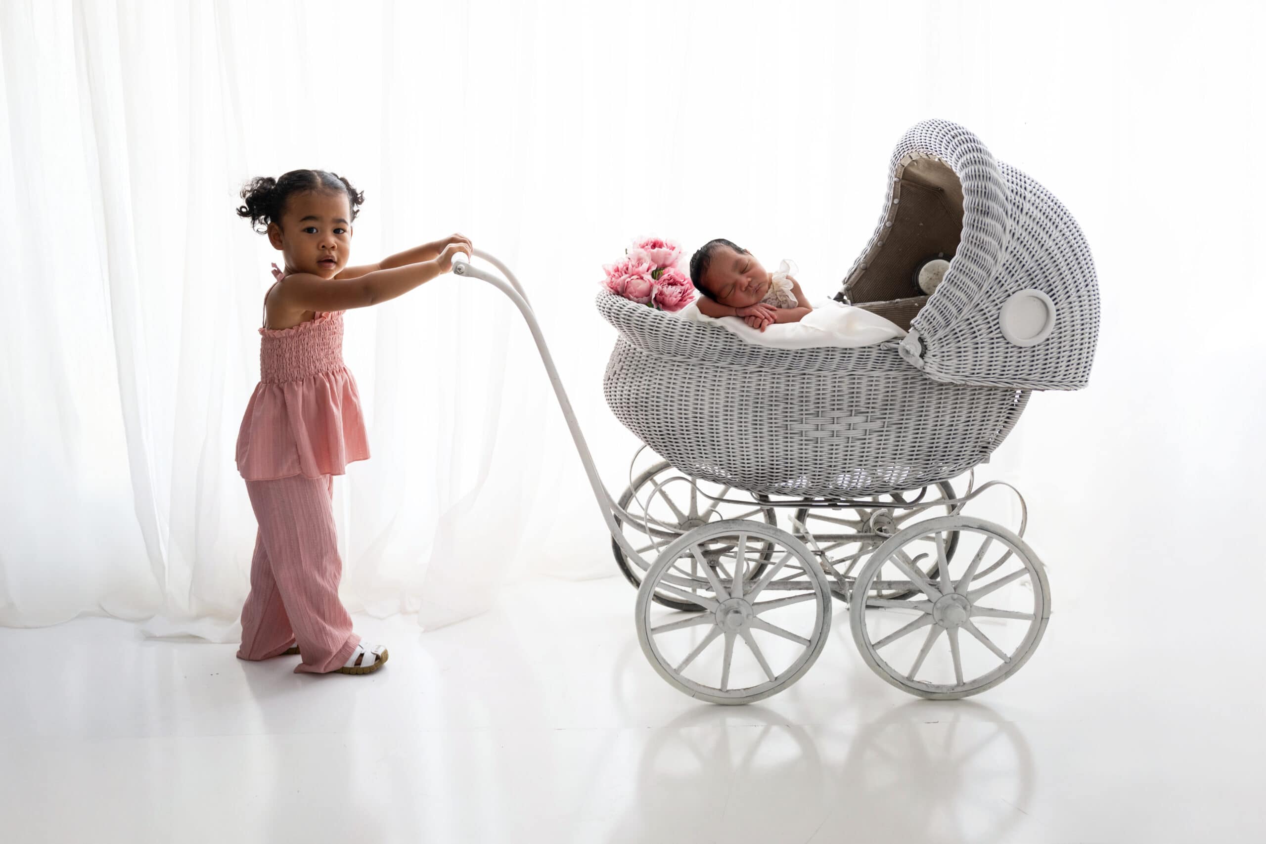 Toddler holding a baby carriage with newborn asleep in it.