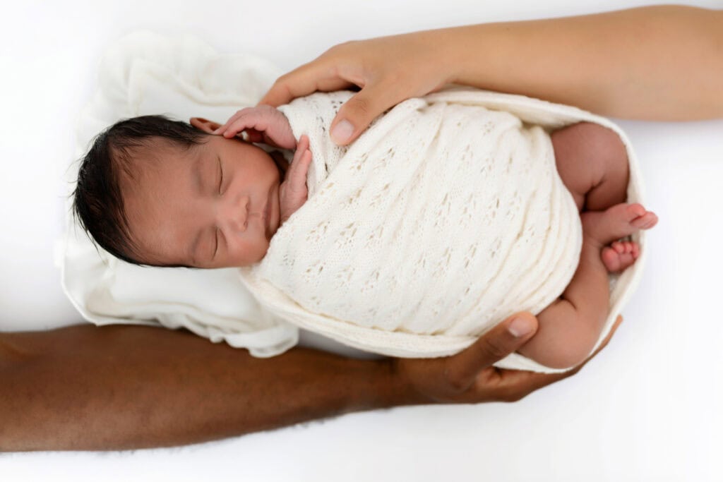 Infant laying on her back while two hands on either side hold her.