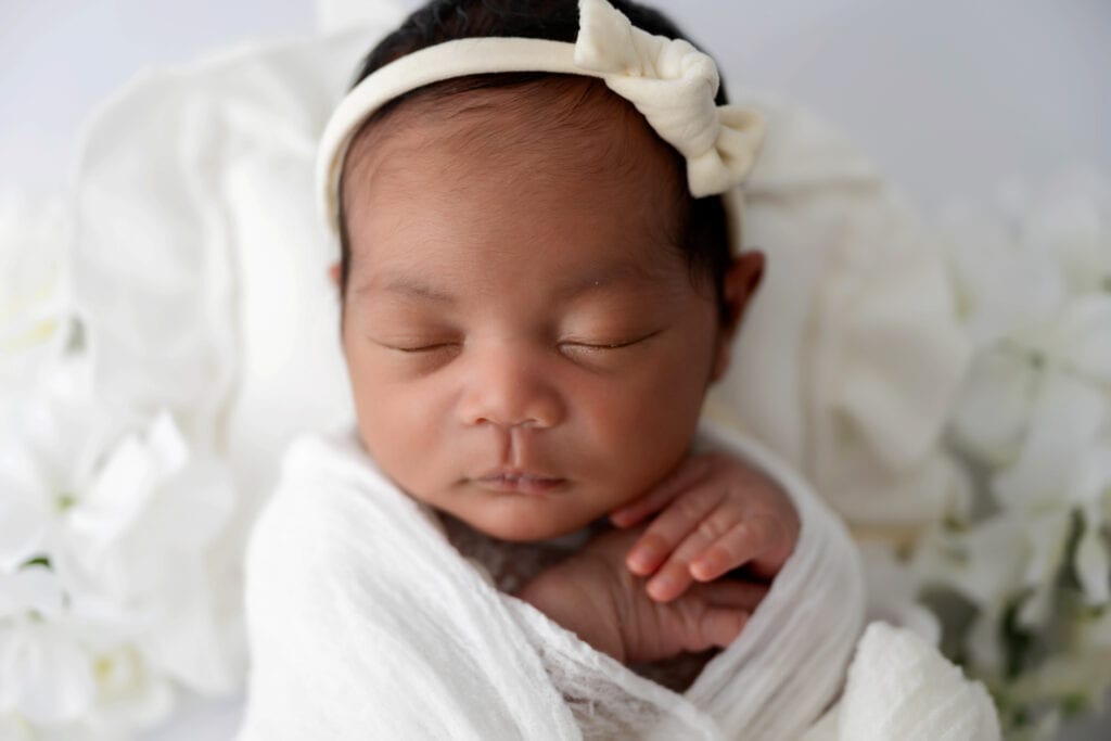 baby with hands under chin, wrapped in a white fabric, sleeping.
