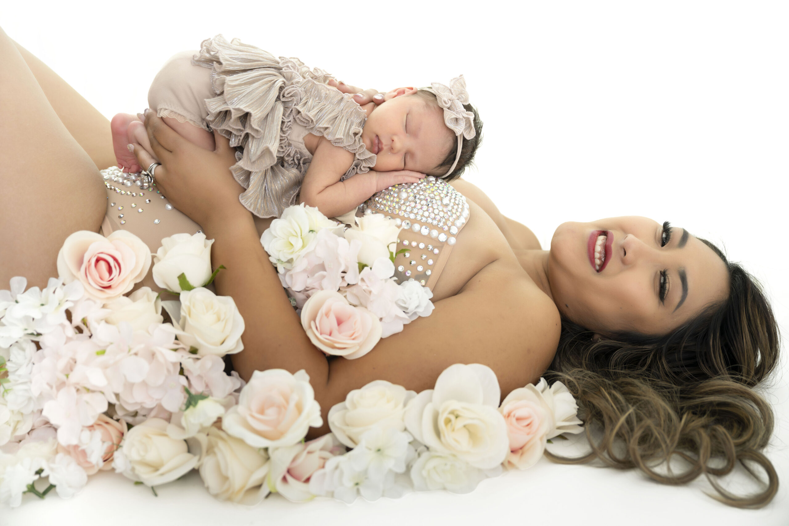 Woman in a rhinestone bodysuit lays on her back as baby lays on top sleeping.