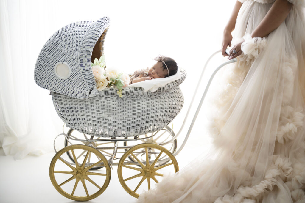 Baby lays in belly inside a vintage stroller while mom stands nearby.