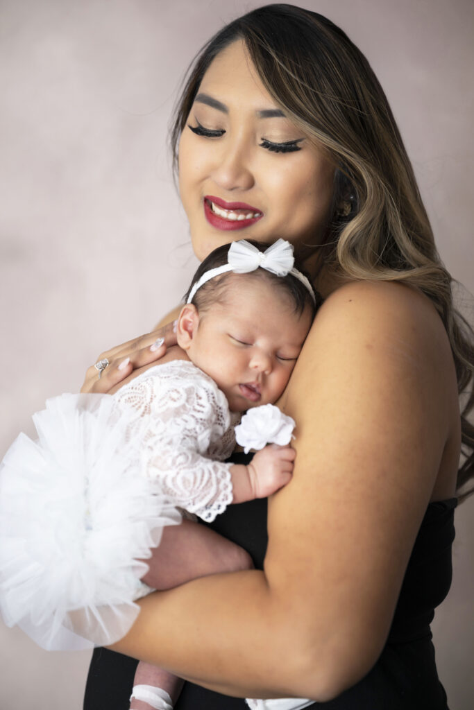 Mother smiles tenderly as she holds a newborn baby in a white tutu inside a photo studio in Chicago.